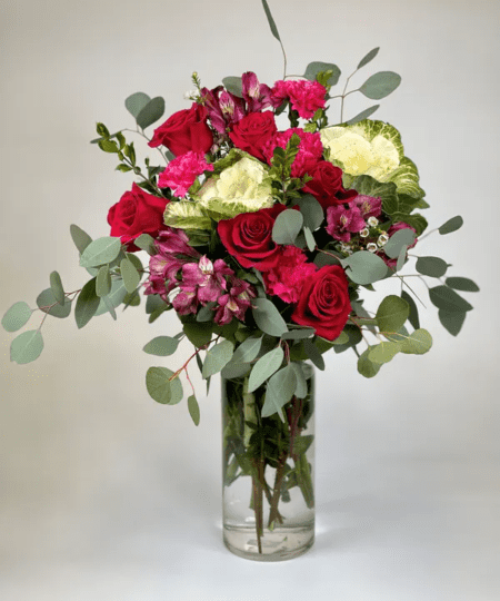 A colorful vase is overflowing with an abundant mix of flowers including lilies, roses, alstromeria, flowering kale, wax flower in a fragrant bed of myrtle and silver dollar eucalyptus. Awesome!